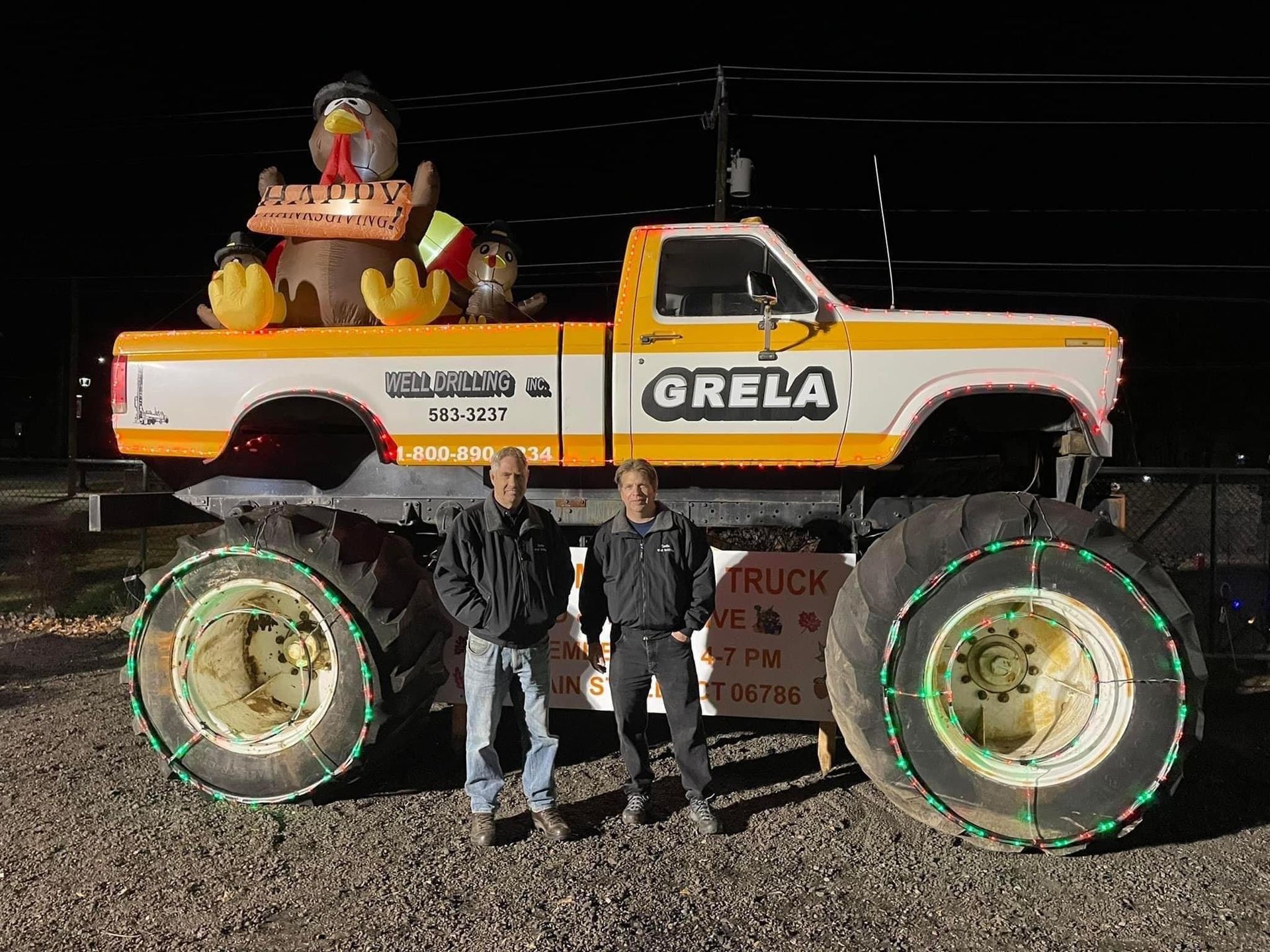 Two men are standing in front of a monster truck with a turkey on the back.