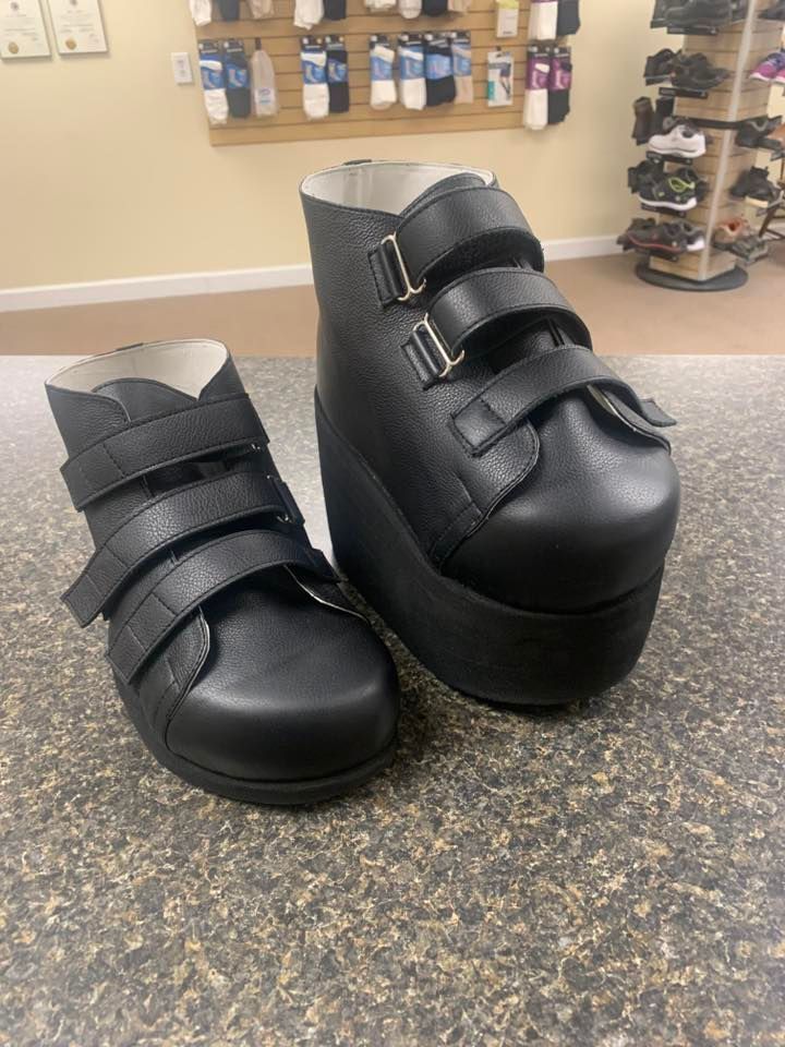 Two black orthopedic shoes on a speckled countertop. One shoe is much larger than the other.
