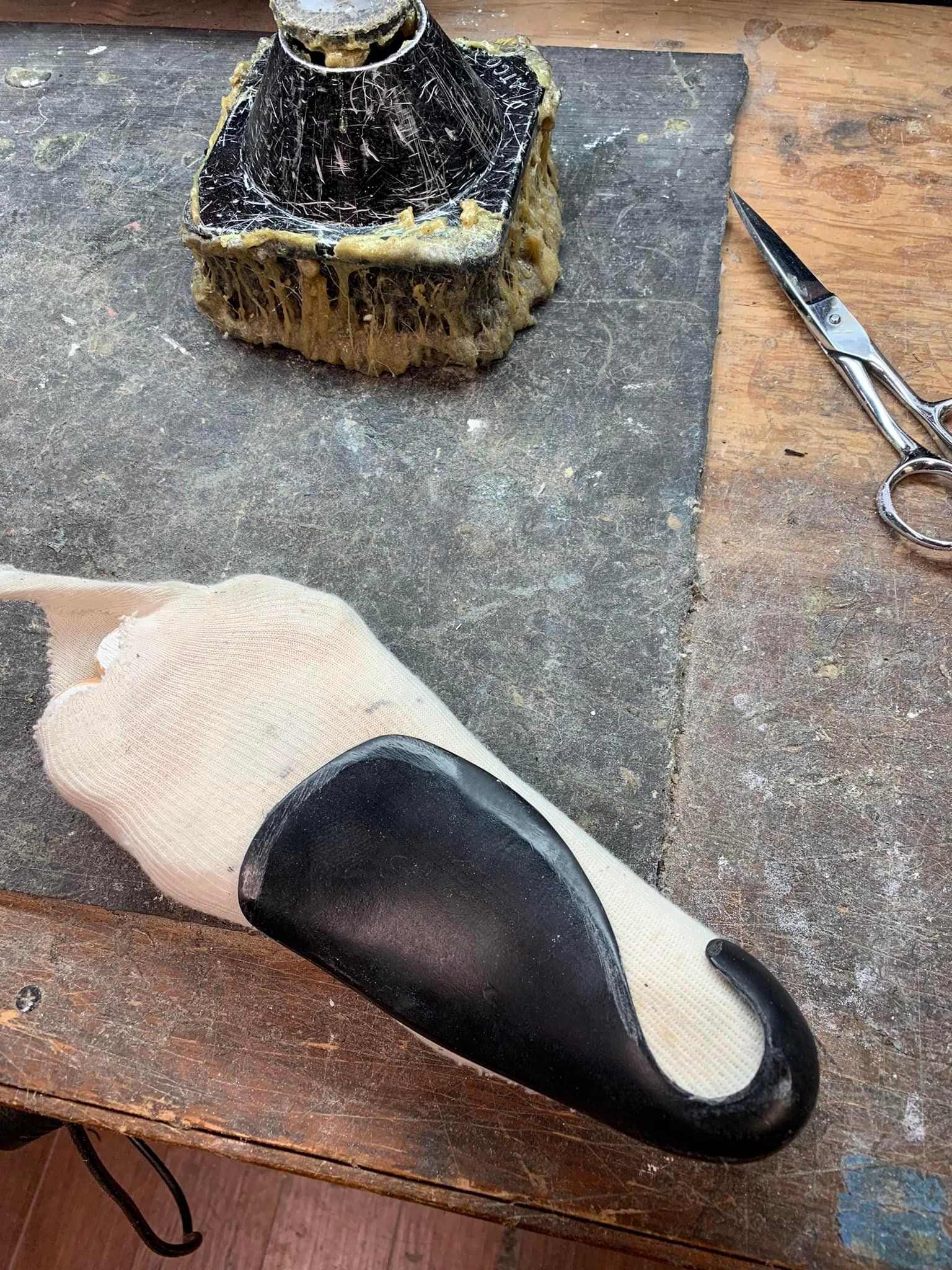 Shoemaking worktable with a foot-shaped form, black leather sole piece, inkwell, and scissors.