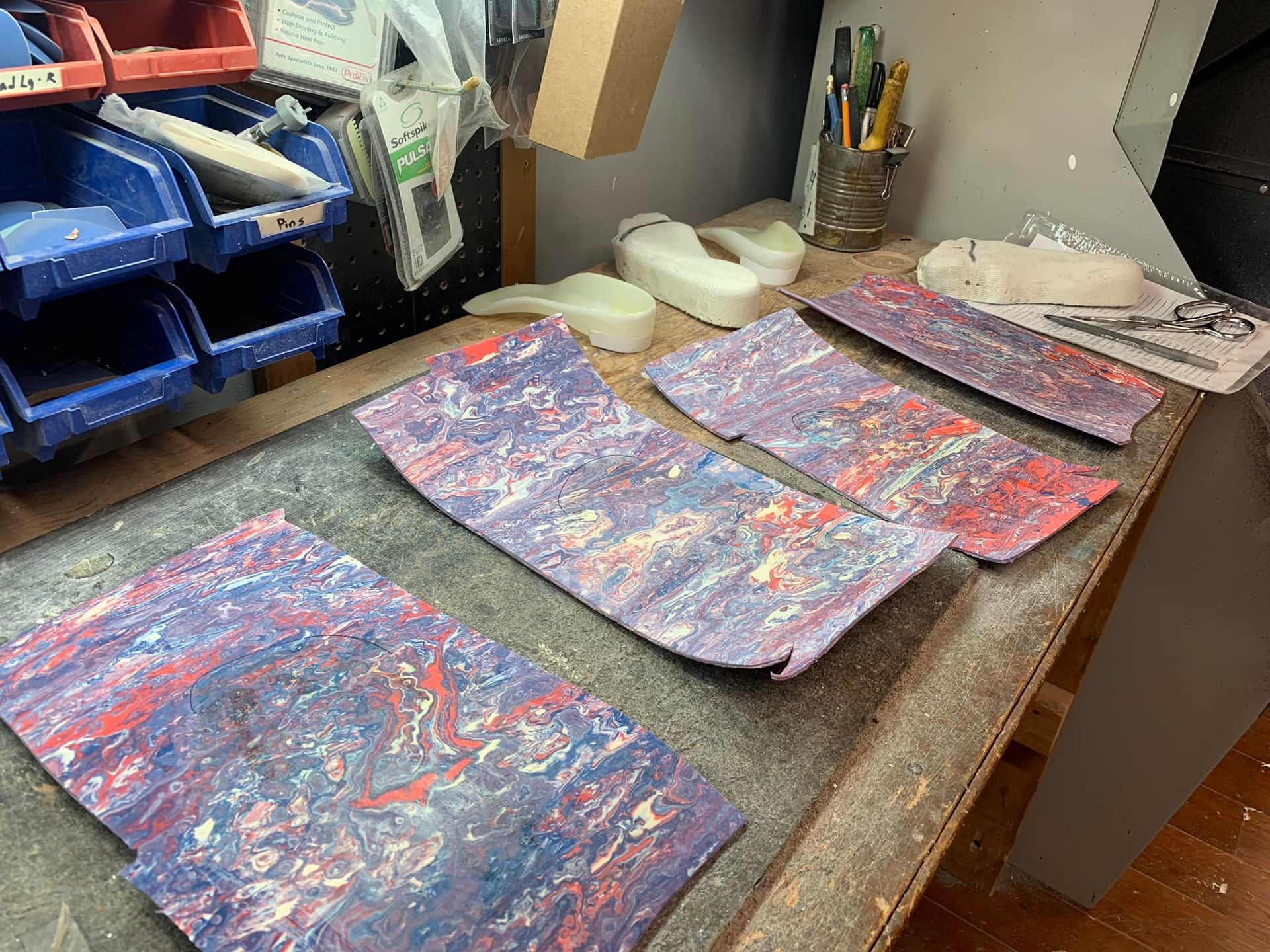 Multicolored painted rectangular pieces on a work table, with tools and storage bins visible.