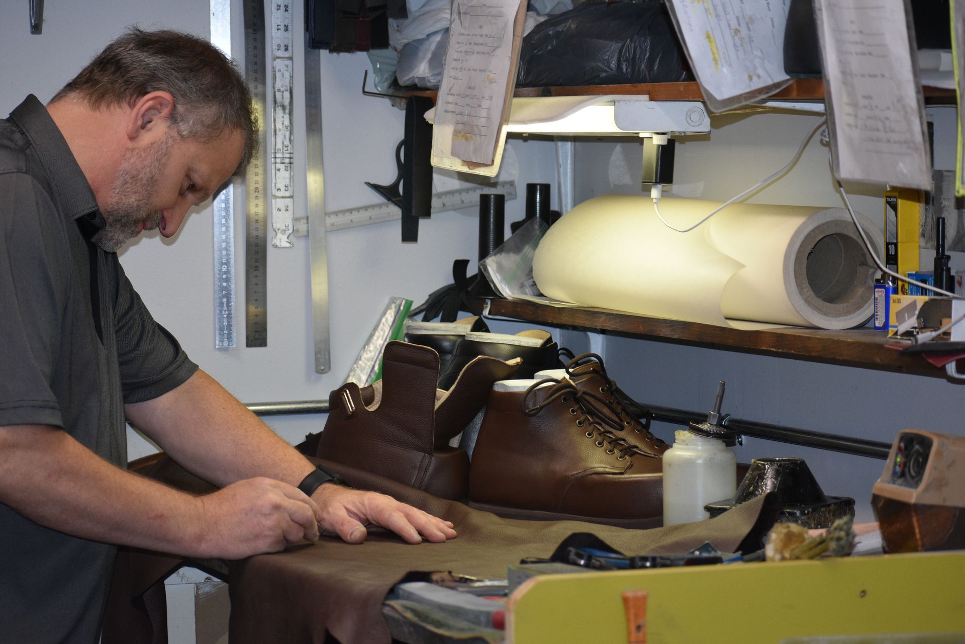 Shoemaker cutting leather near brown boots in a workshop.