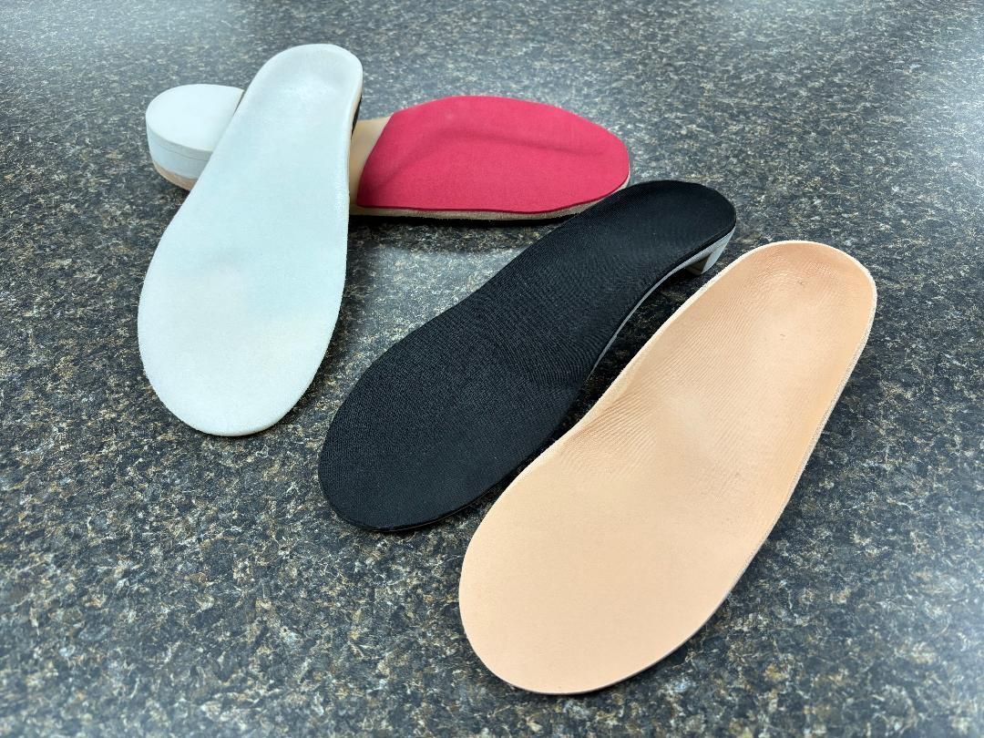 Foot orthotics in various colors, including white, black, tan, and red, on a speckled surface.