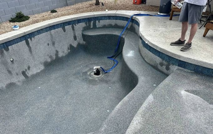 An empty, speckled-gray swimming pool with a blue tile border and a drainage fixture in the floor.