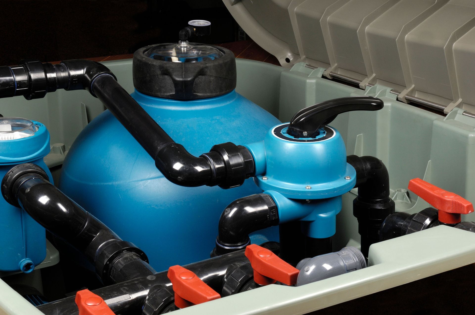 A blue pool sand filter system with black piping and several orange handle valves inside an open protective enclosure.