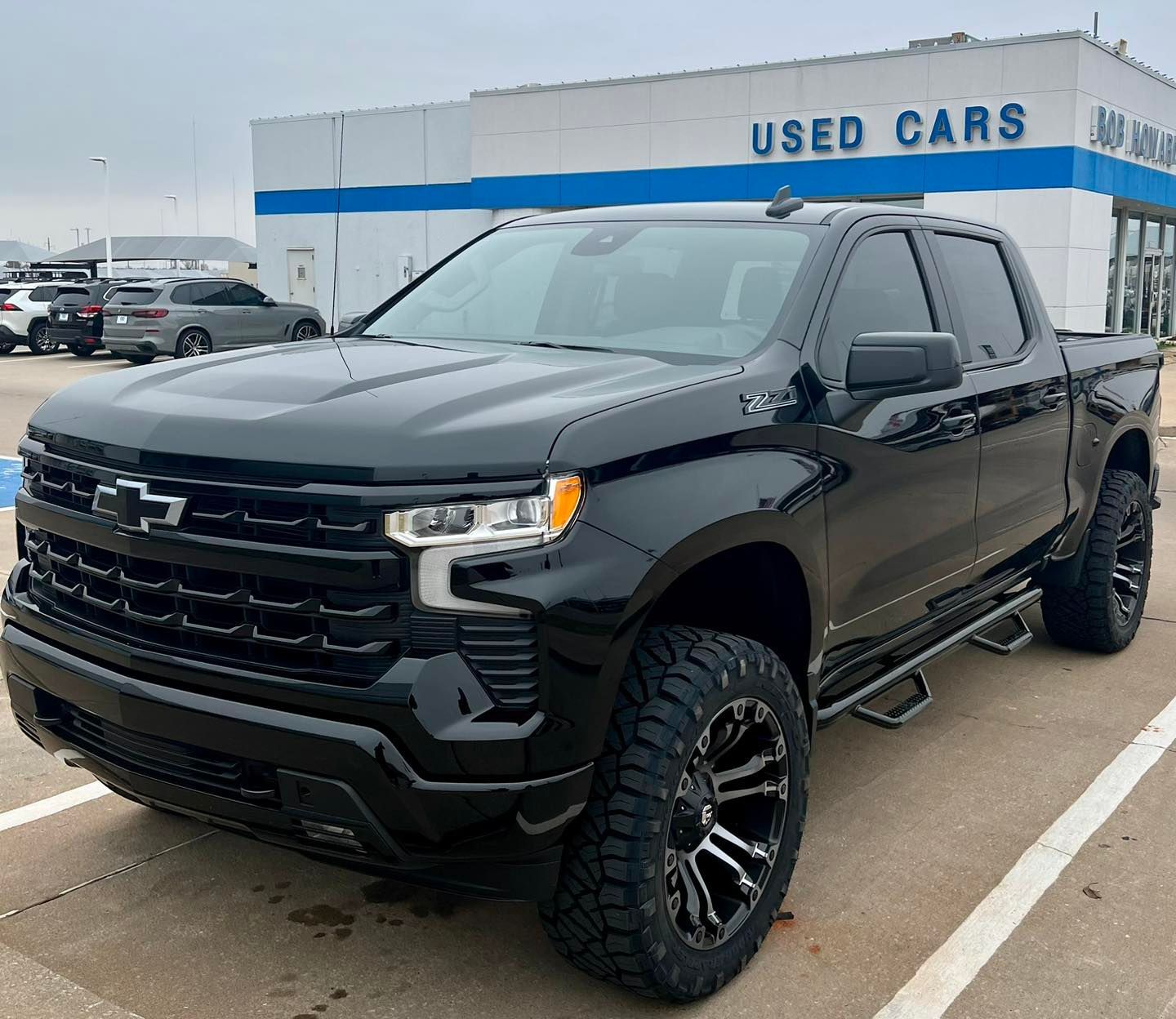 A black truck is parked in front of a used car dealership