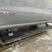A gray truck with a black side step is parked in a garage
