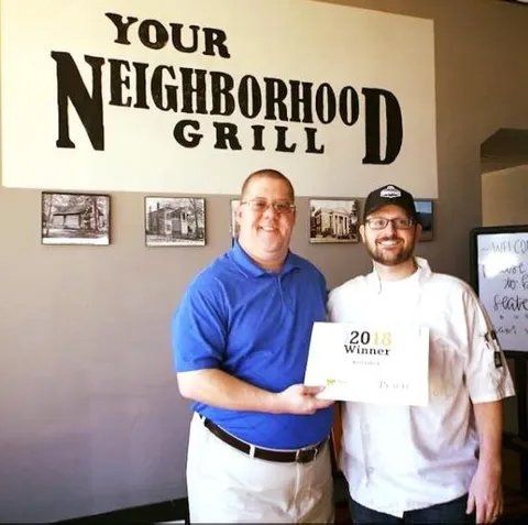 Two men standing in front of a sign that says your neighborhood grill