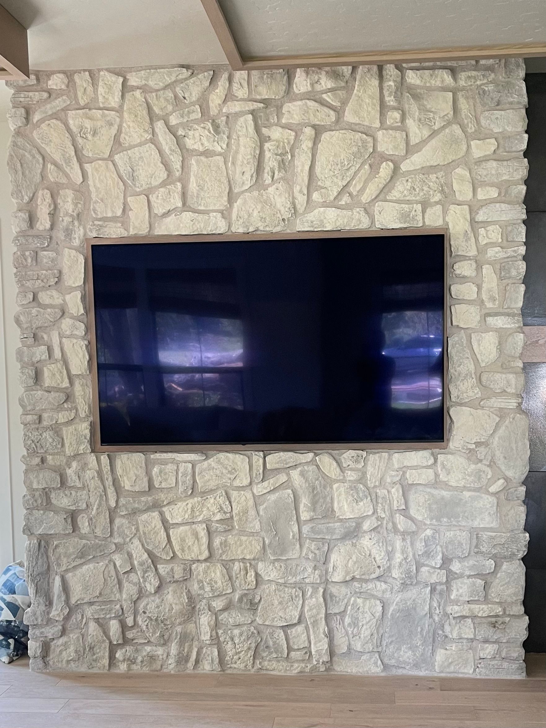 A flat screen tv is mounted on a stone wall in a living room.