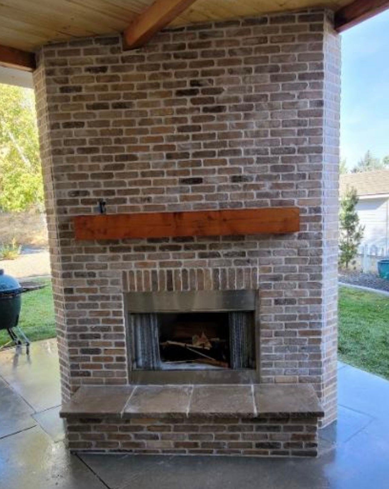A large brick fireplace with a wooden mantle on a patio.