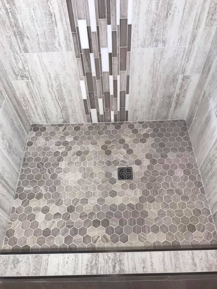 A shower stall with a hexagonal tile floor and a drain.