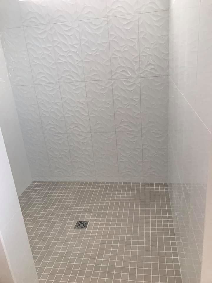 A walk in shower with white tiles and a drain.