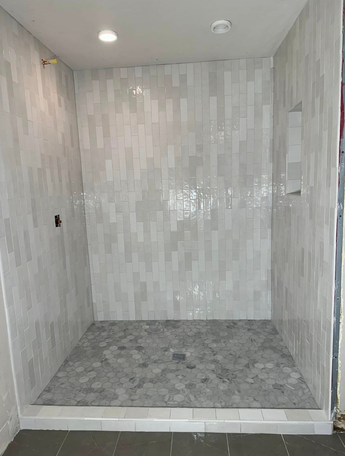 A walk in shower with white tiles and a gray tile floor.