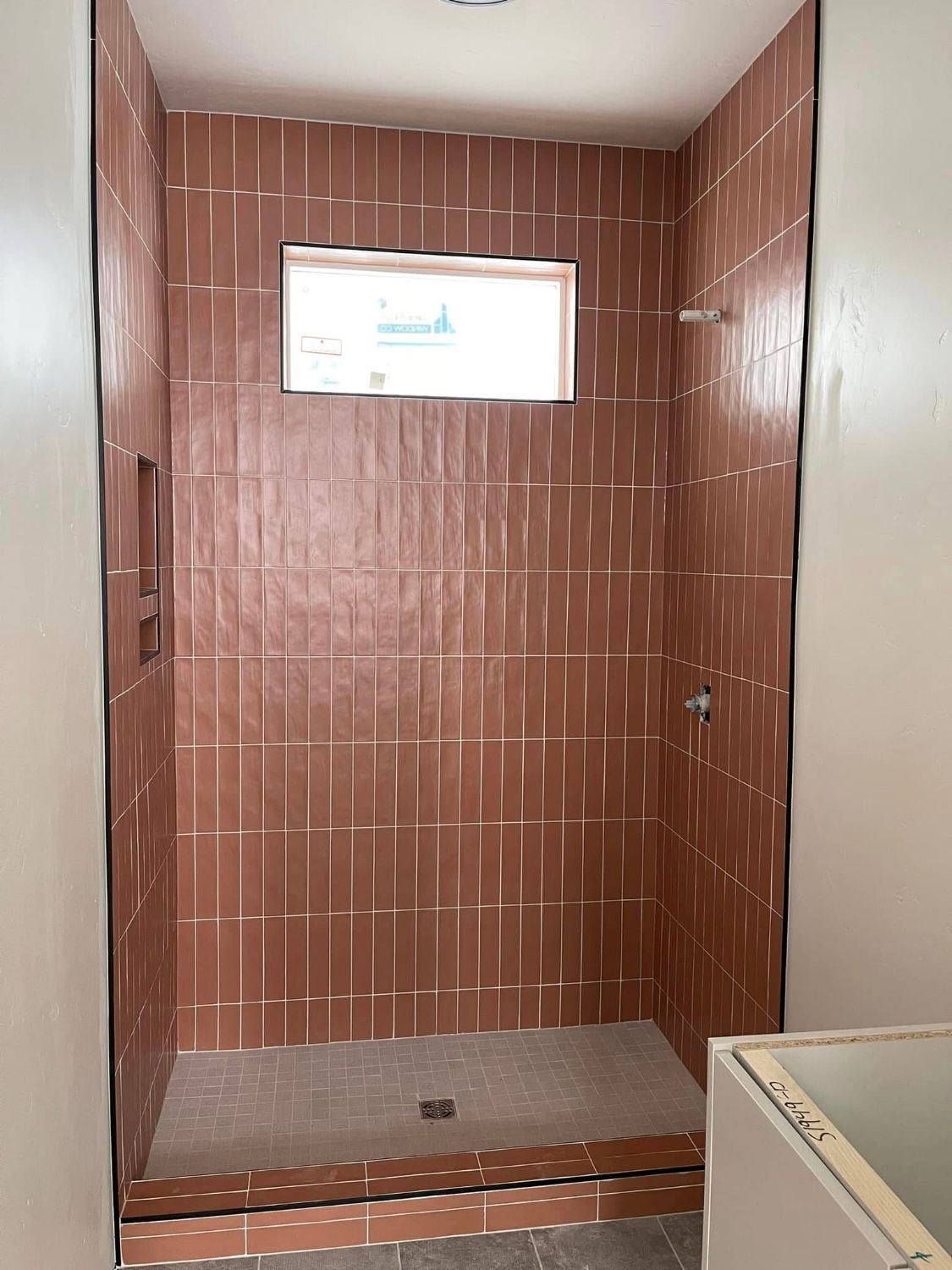 A shower stall with red tiles and a window in a bathroom.