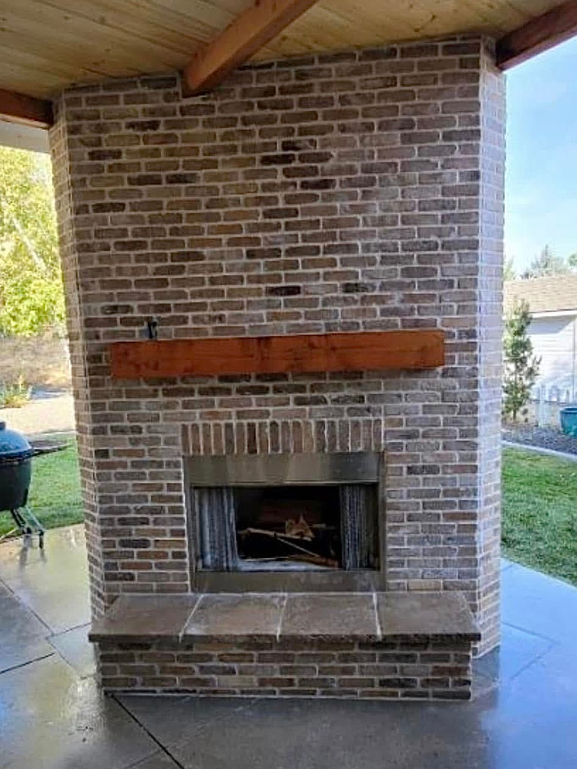 A large brick fireplace with a wooden mantle on a patio.