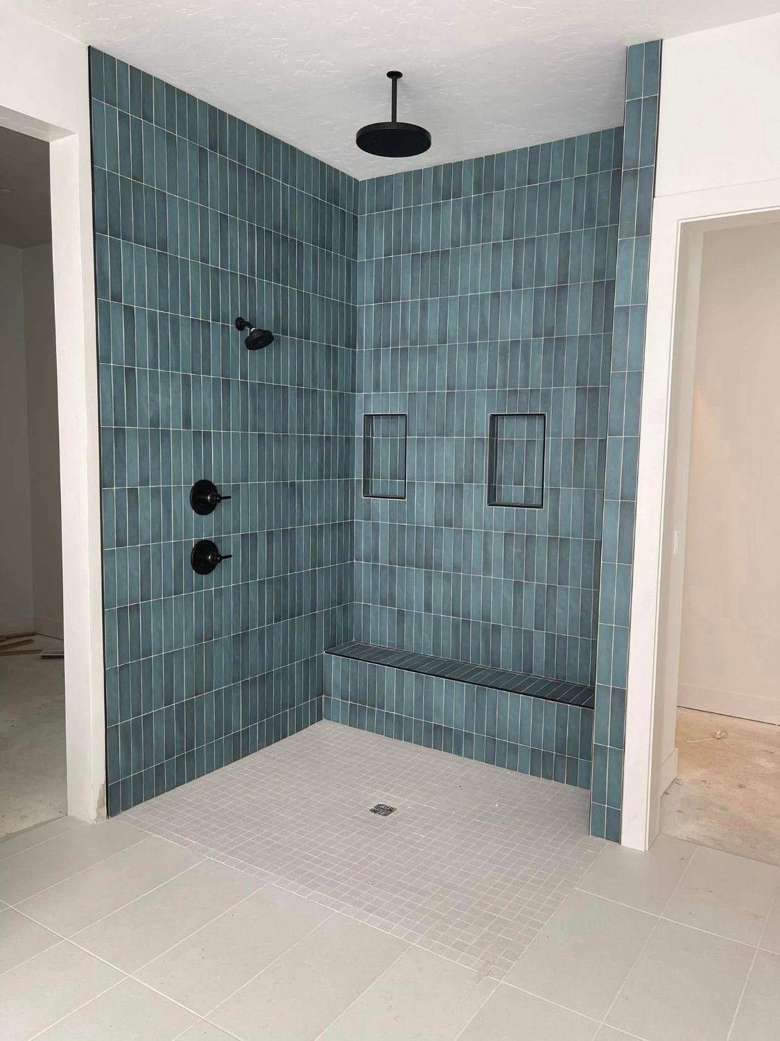 A bathroom with a walk in shower with blue tiles and a bench.