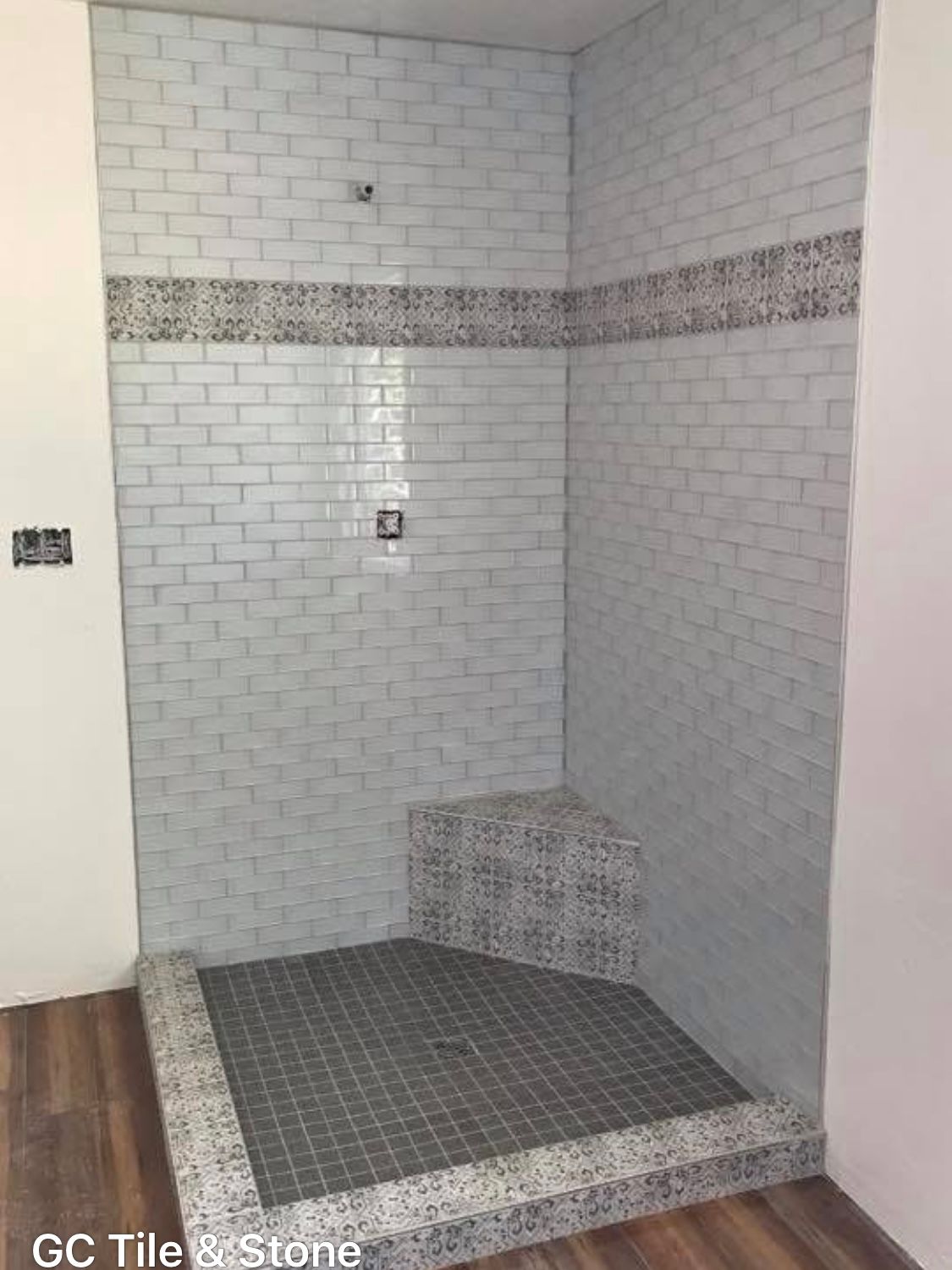 A walk in shower with white tiles and a wooden floor.