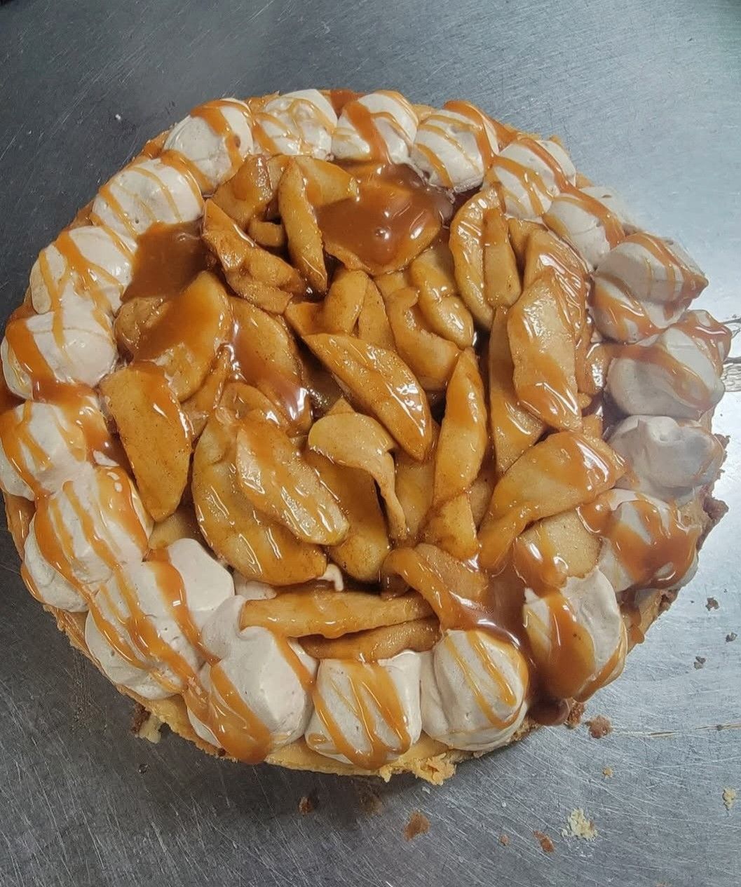 An apple pie with caramel sauce and whipped cream on a table