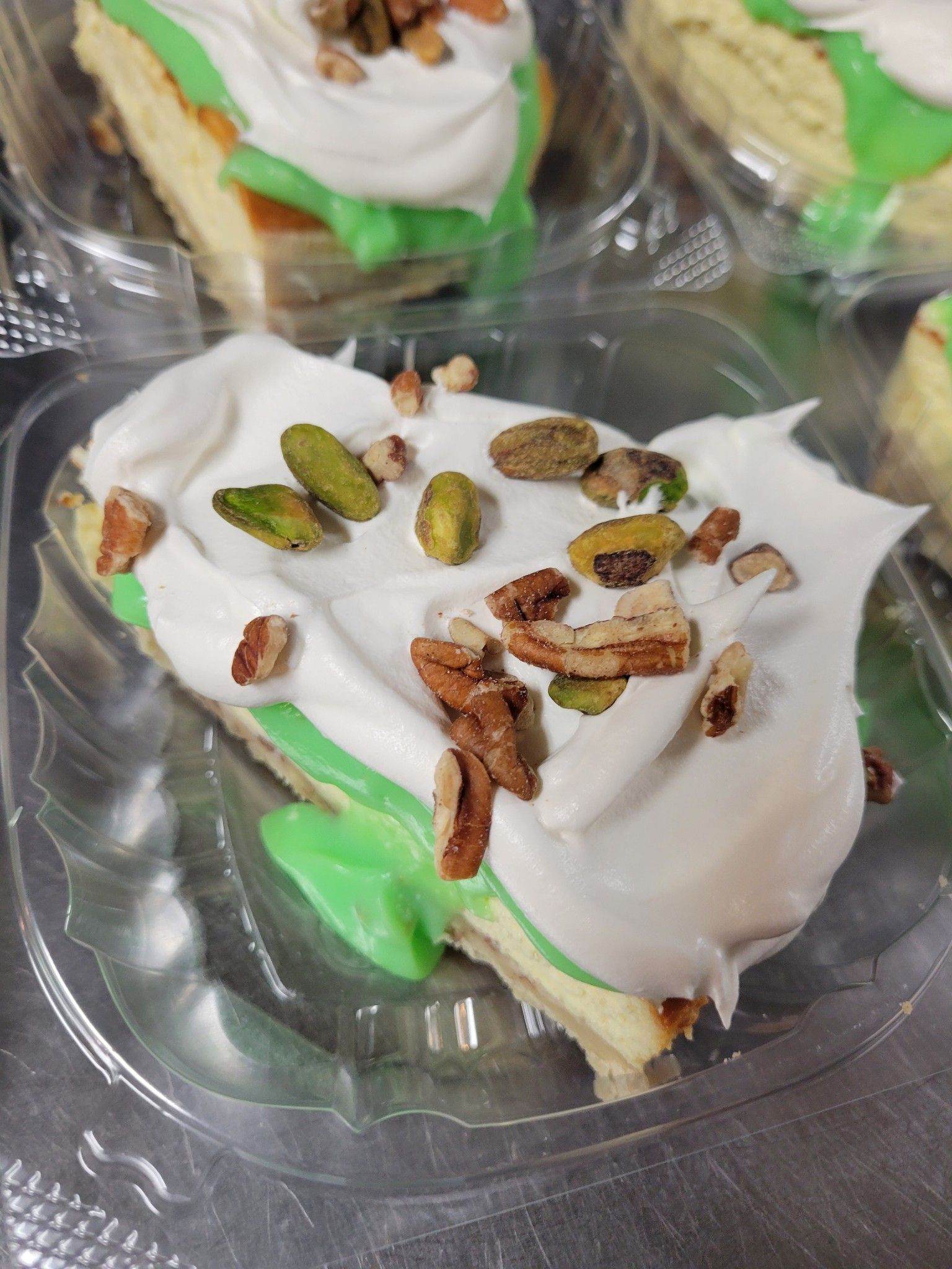 A piece of cheesecake with green frosting and pistachios in a plastic container