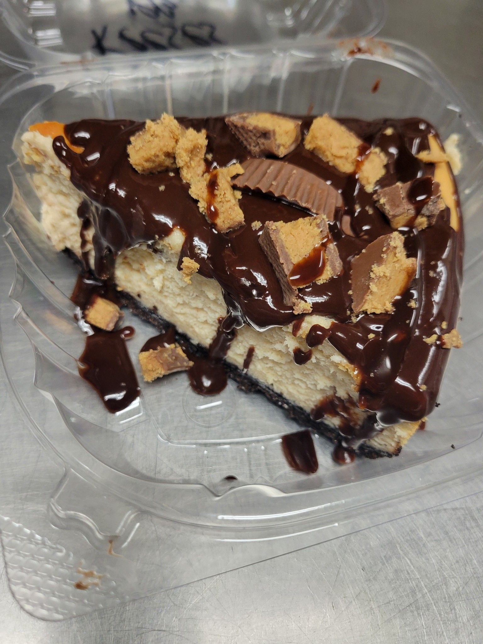 A slice of cheesecake with chocolate sauce and peanut butter cups in a plastic container