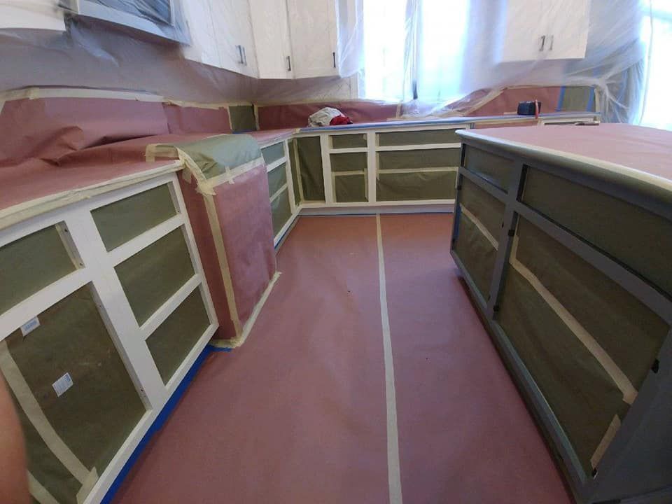 Kitchen cabinets and countertops covered with masking paper and tape, ready for painting.