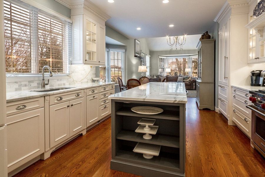 White kitchen with wooden floors, island with marble countertop, and view into the living room.