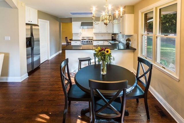 Kitchen and dining area with round table and chairs. Hardwood floors, white cabinets, stainless steel appliances, and a chandelier.