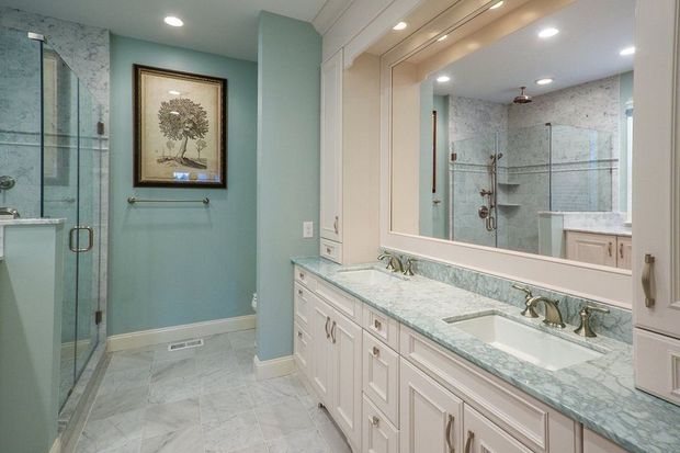 Bathroom with light blue walls, white cabinets, and a large mirror.