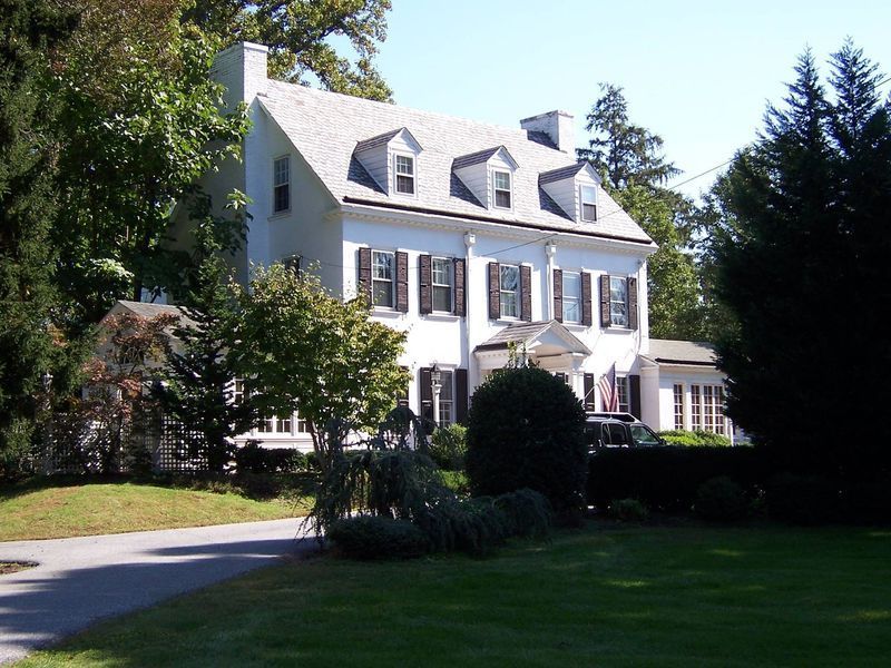 White Colonial-style house with black shutters, green lawn, and a winding driveway.