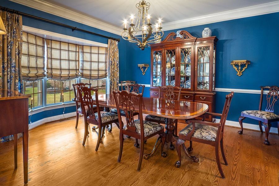 Dining room with a blue wall, round wooden table, chairs, hutch, and chandelier.