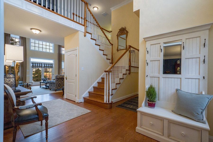 Entryway with staircase, bench, and living room visible. Wooden floors, light walls, and a decorative mirror.