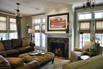 Cozy living room with fireplace, brown couches, patterned ottoman, and window with shades.