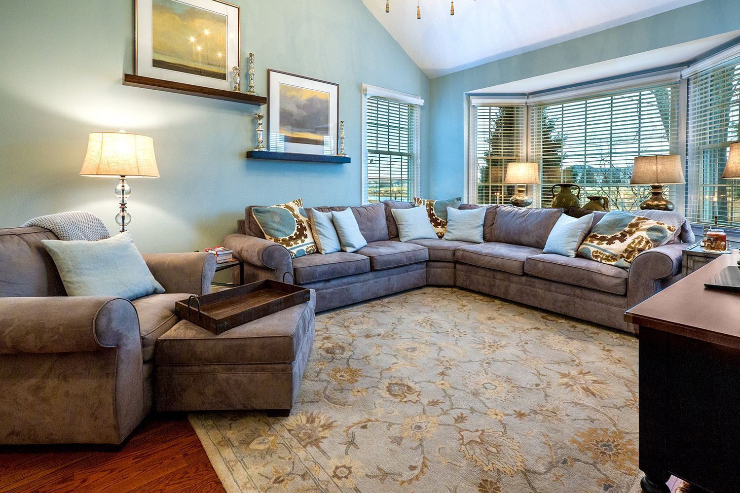 Living room with a large gray sectional sofa, ottoman, and area rug. Bay window, blue walls.