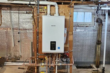 A water heater is installed in a basement next to a brick wall.