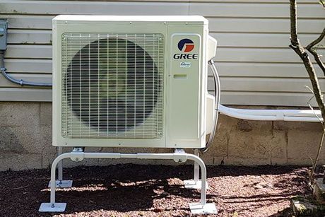 A gree air conditioner is mounted to the side of a house.