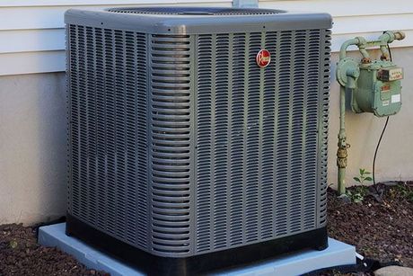 A gray air conditioner is sitting outside of a house.