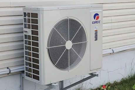 A gree air conditioner is mounted on the side of a house.