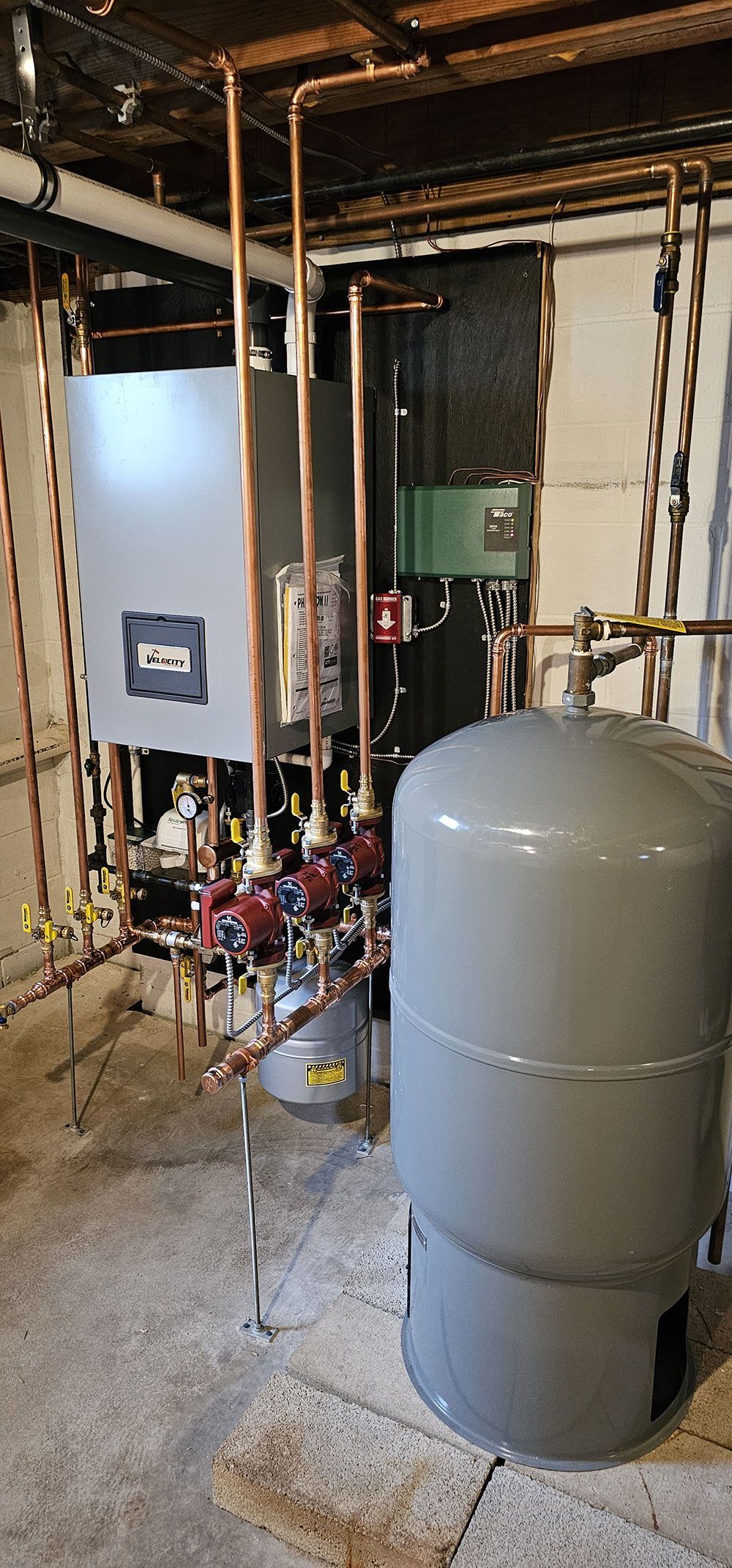 A boiler is sitting in a basement next to a tank.