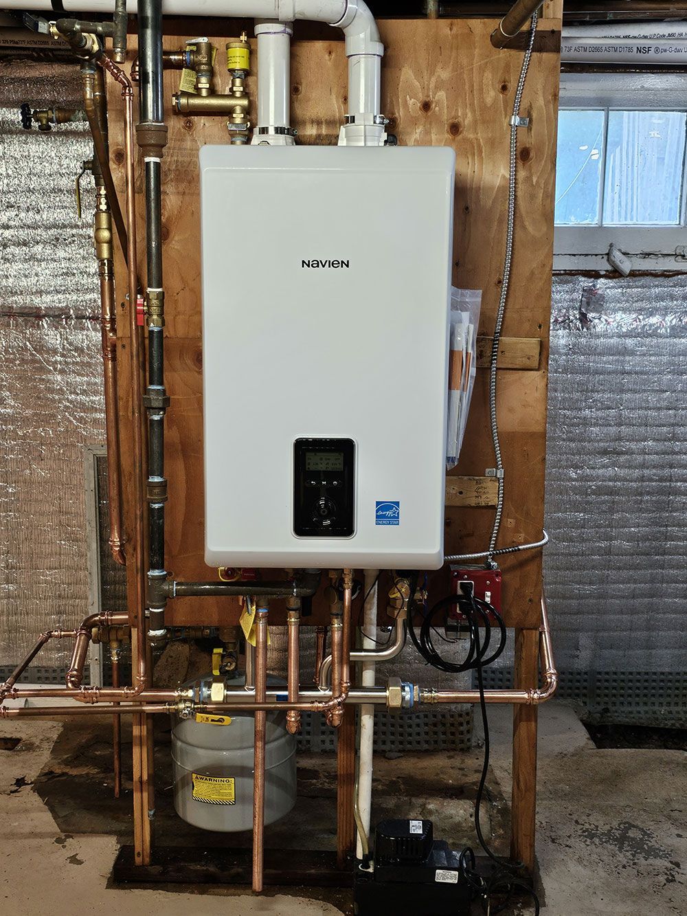 A white water heater is mounted to a wooden wall.