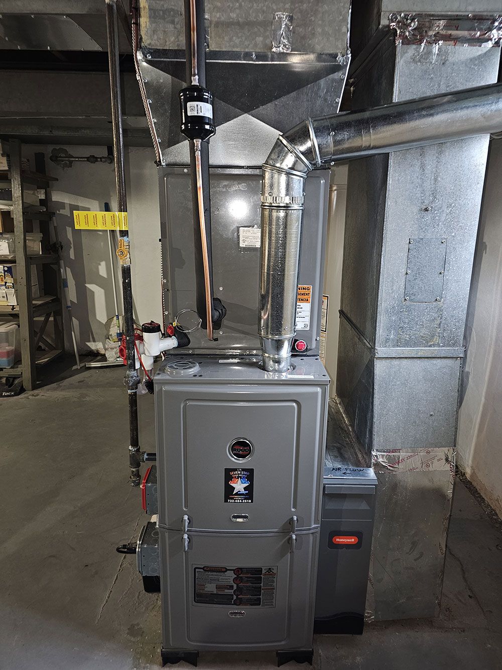 A furnace is sitting in a basement next to a wall.