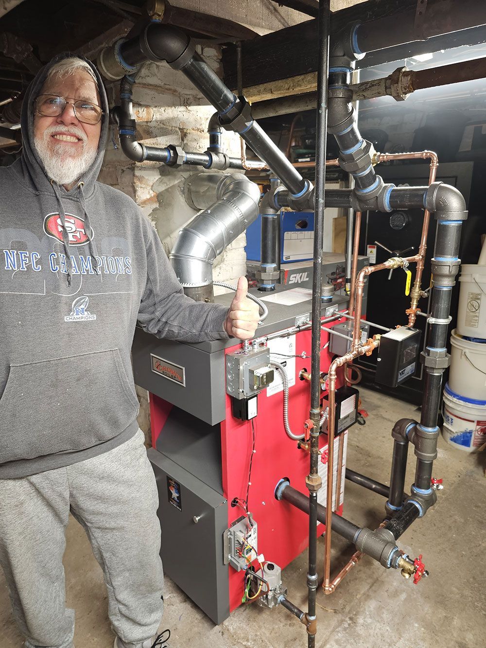 A man is standing next to a red boiler in a basement.