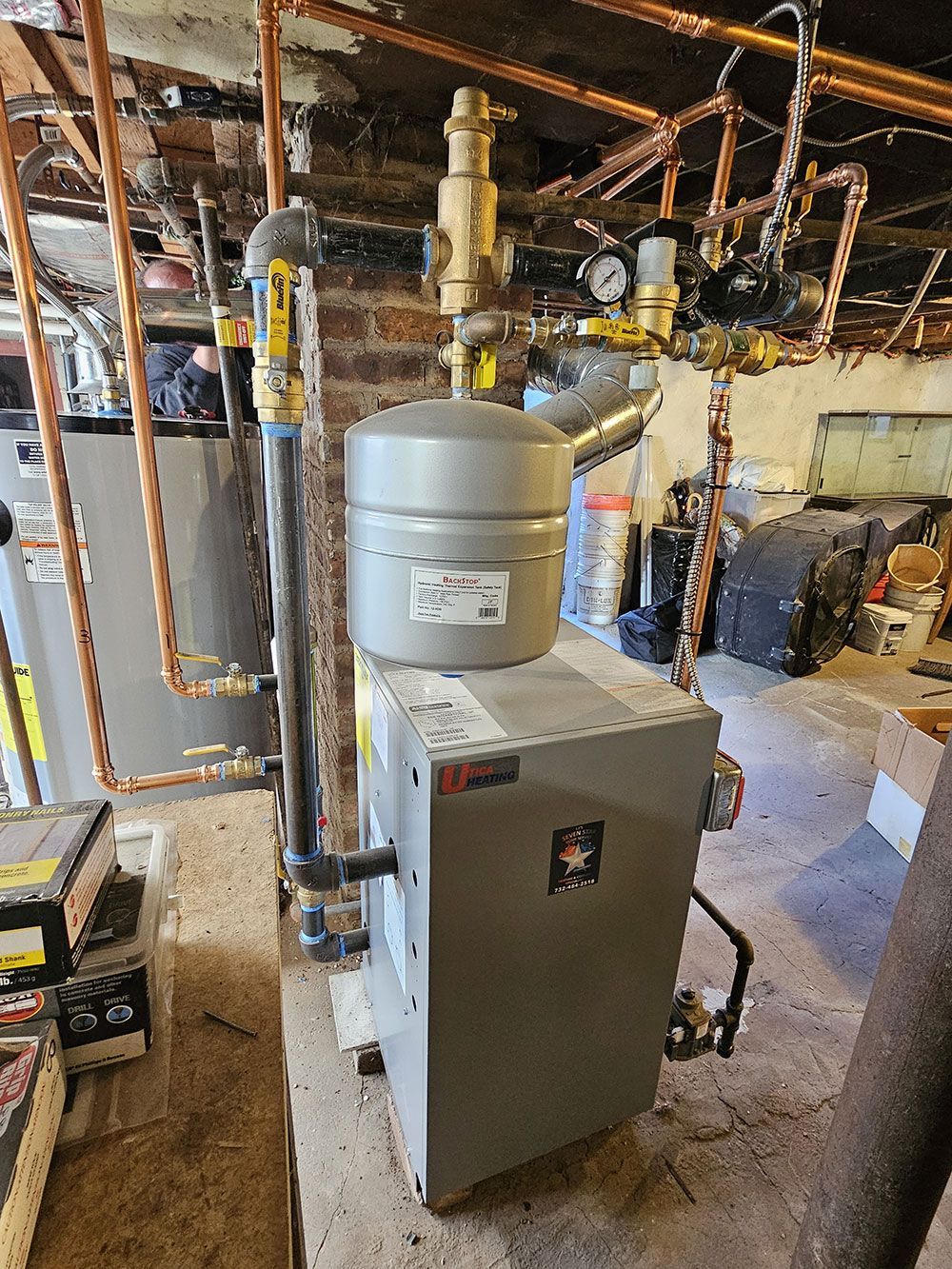 A boiler is sitting in a basement next to a water heater.