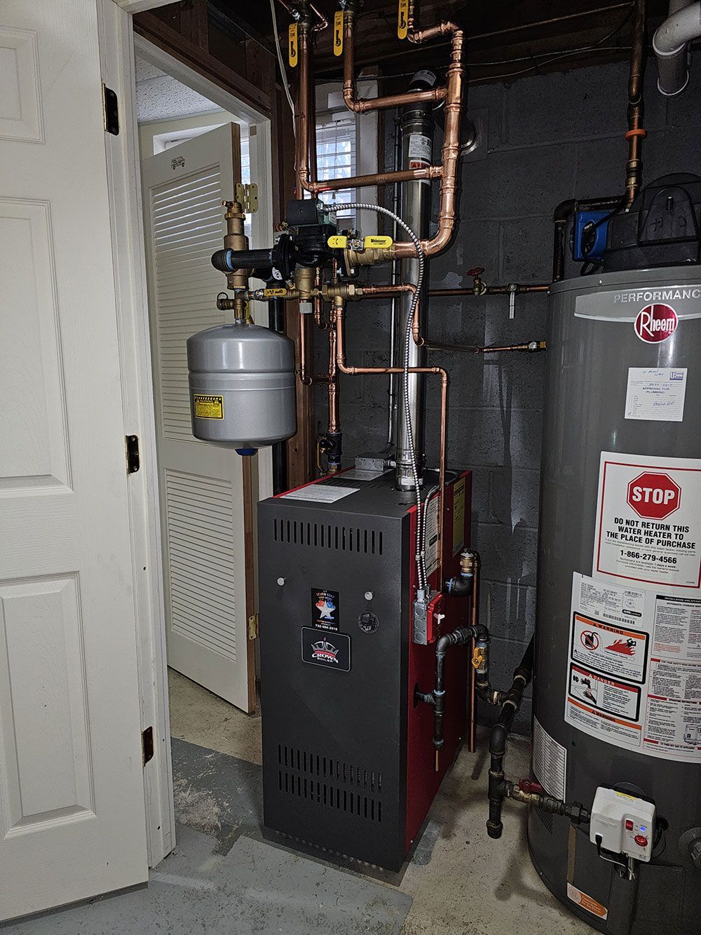 A boiler and a water heater are in a basement.