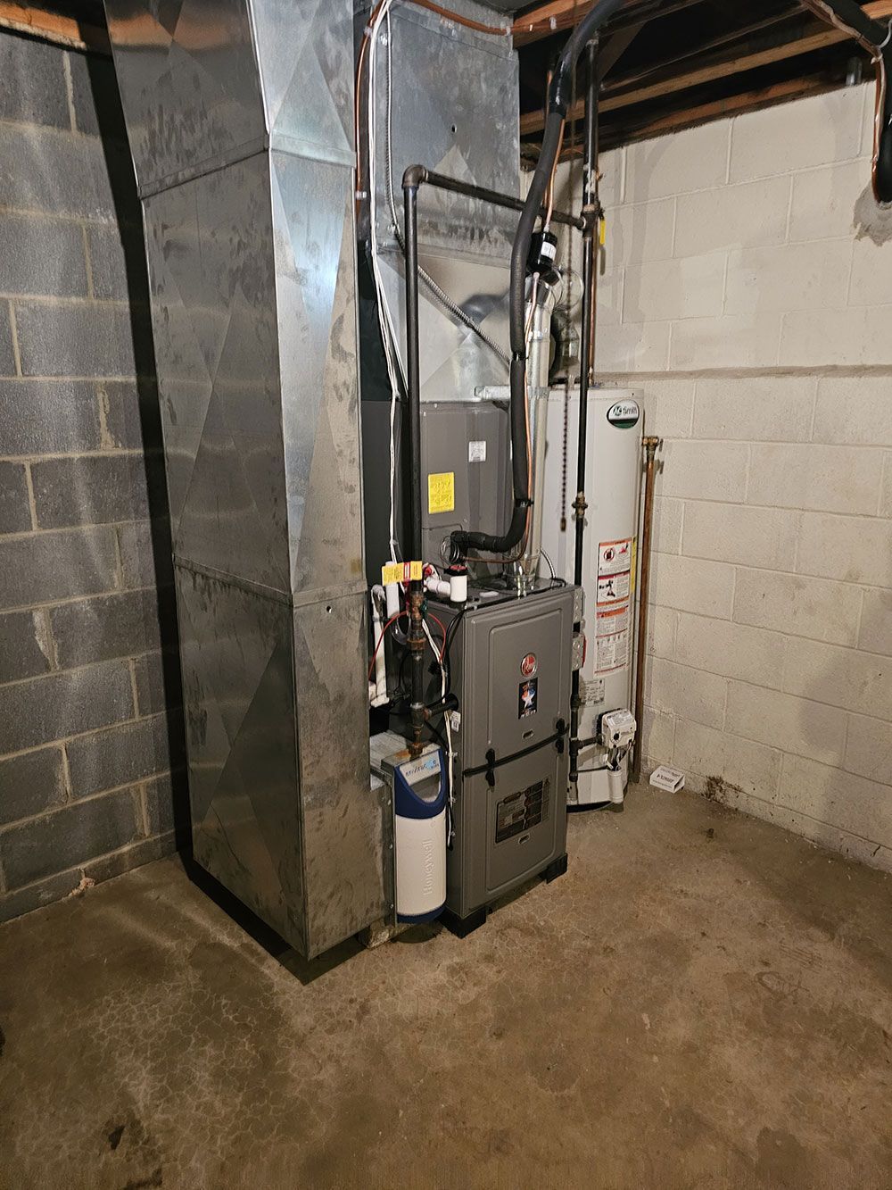 A furnace is sitting in a basement next to a water heater.
