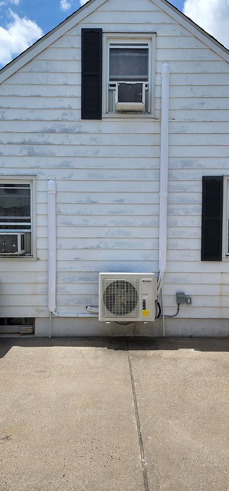 A white house with black shutters and a white air conditioner on the side of it.