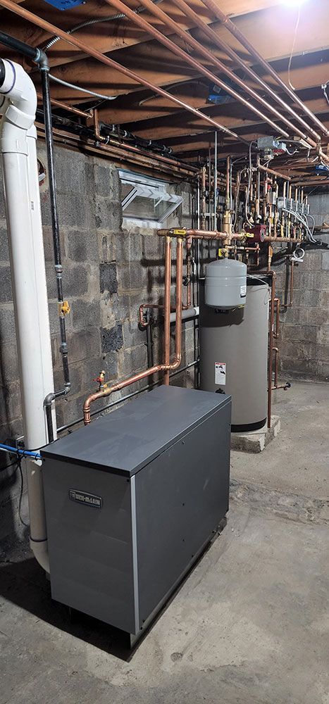 A boiler is sitting in a basement next to a water heater.