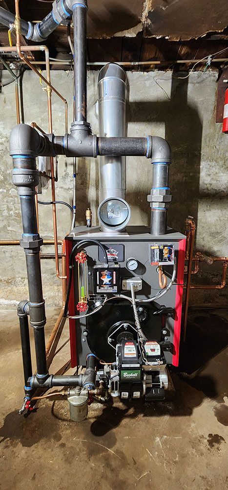 A red and black boiler is sitting in a basement next to pipes.