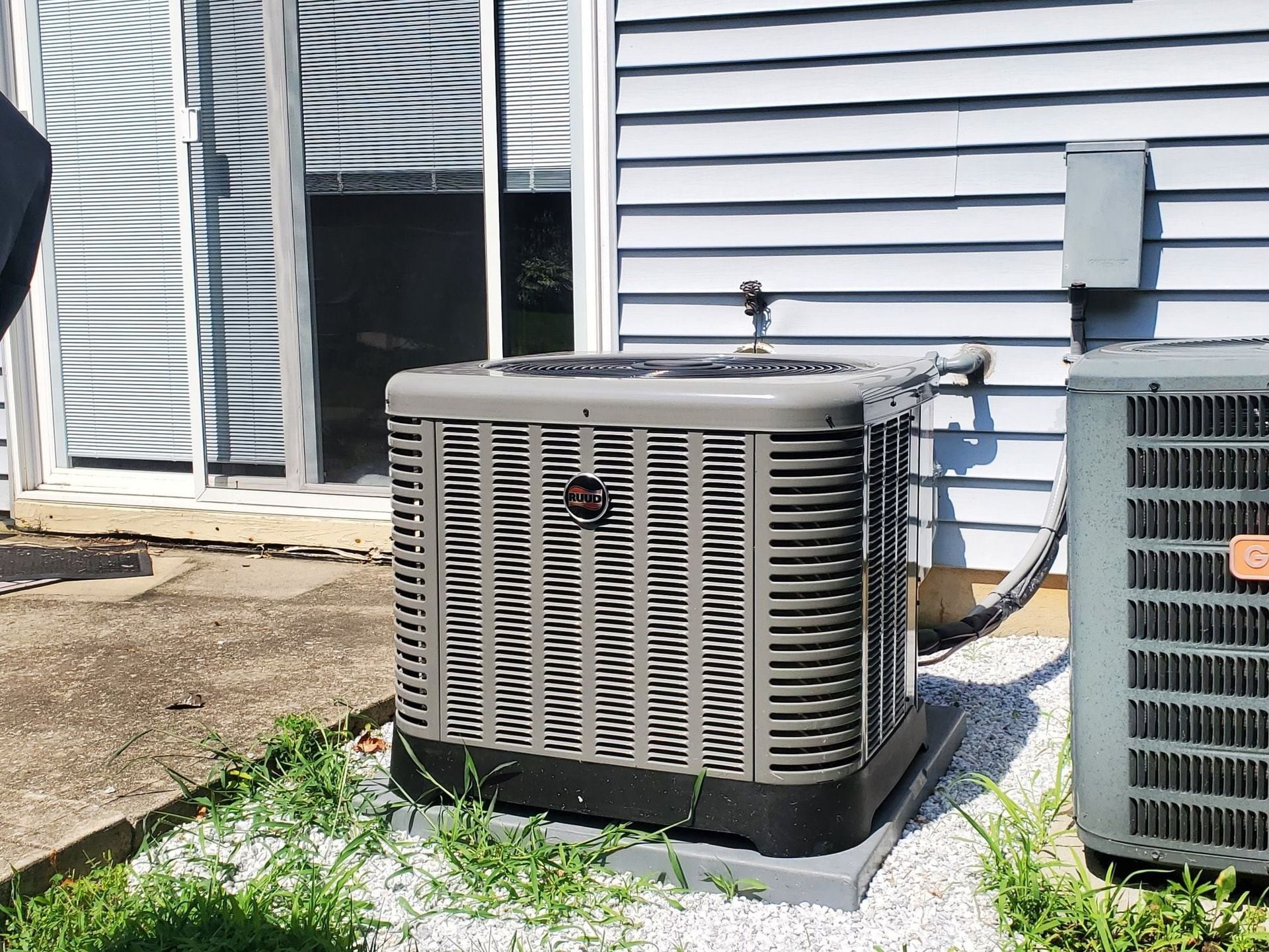 Two air conditioners are sitting outside of a house.