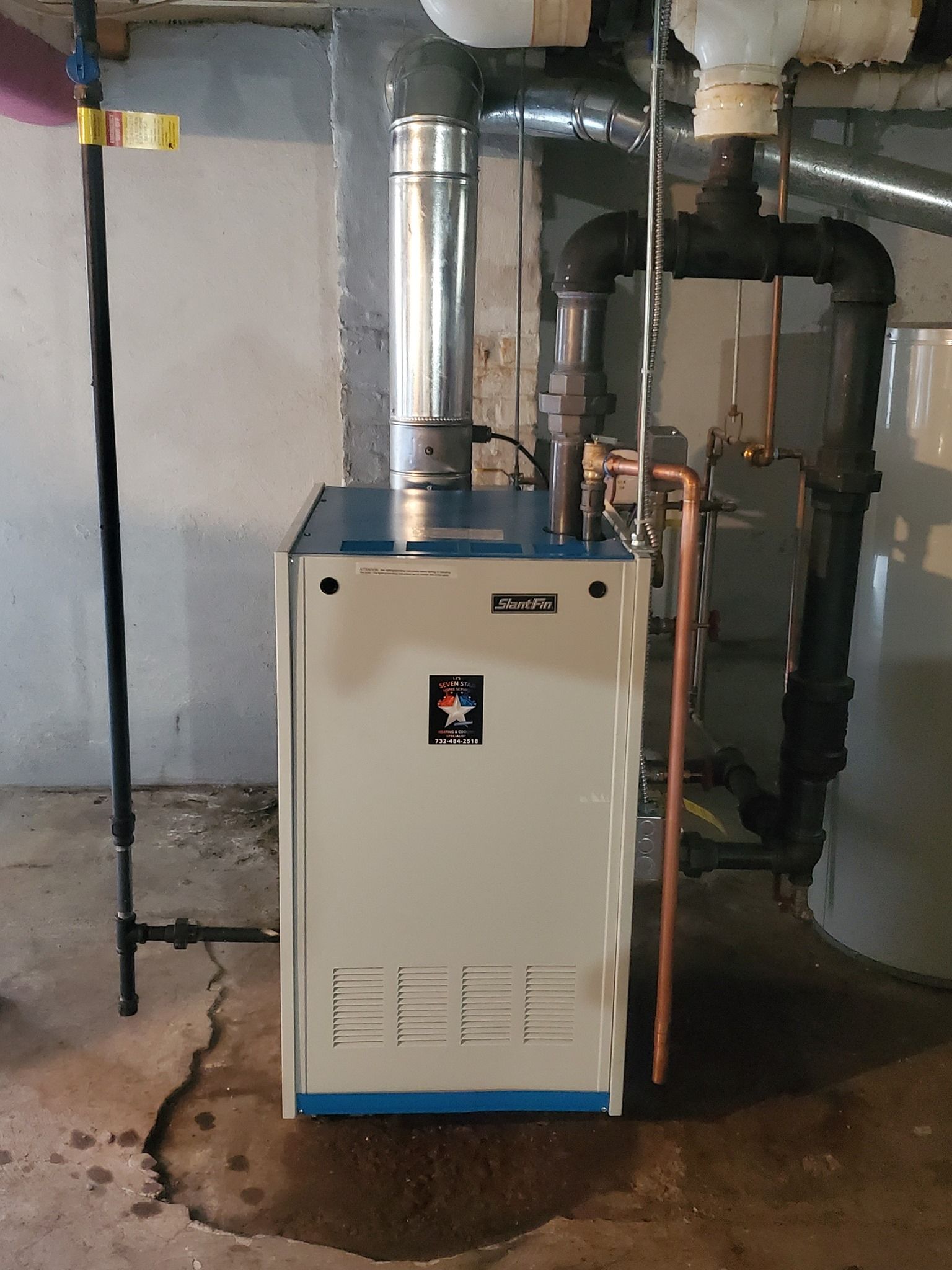 A blue and white boiler in a basement with copper pipes