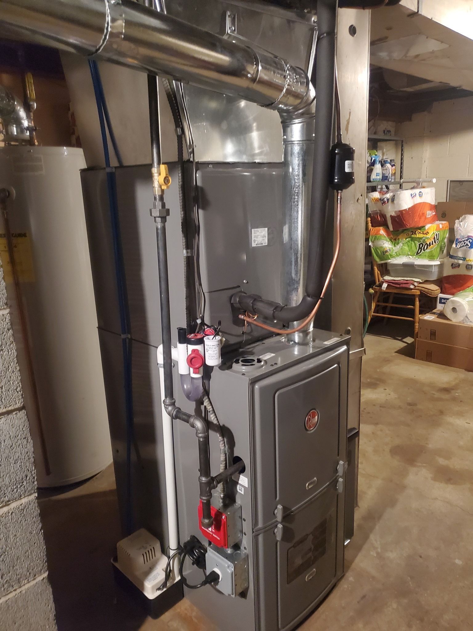 A furnace is sitting in a basement next to a water heater.
