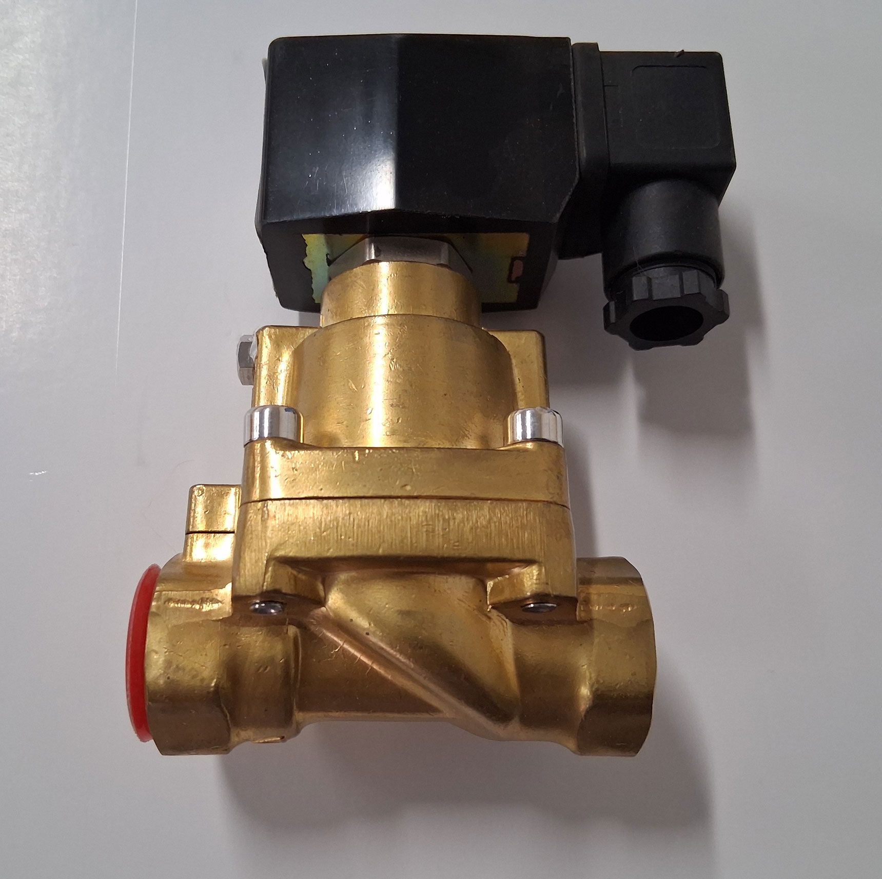 Brass solenoid valve with black electrical actuator and red cap on a white background